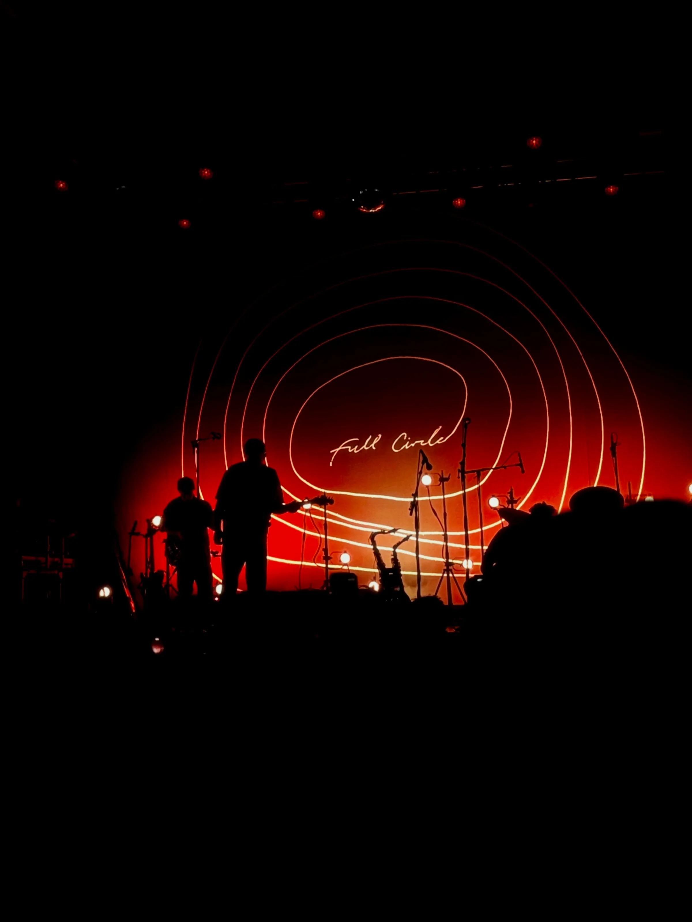 Silhouetted musicians performing in front of a large circular red stage light