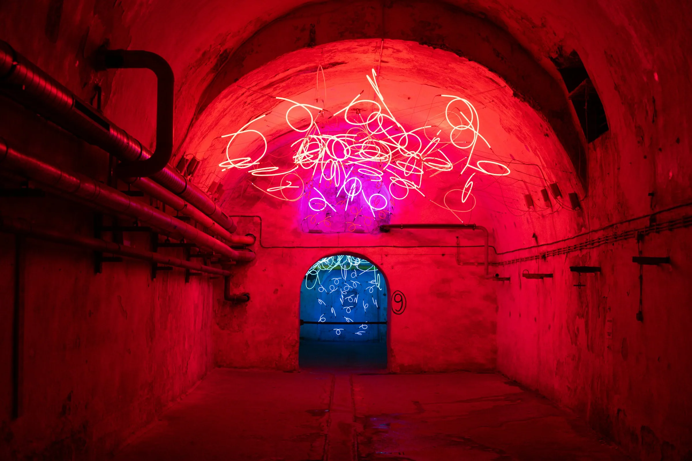 A long tunnel flooded with red neon light, its walls receding into darkness